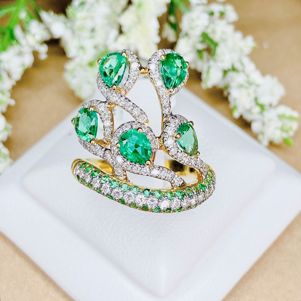 แหวนเพชรไขว้ล้อมมรกต The ring rotates upward. โดยฝังเพชรแถวสลับมรกตที่ตัวเรือนด้านล่าง แล้วค่อยหมุนไต่ระดับขึ้นด้านบนเป็นเหมือนสวนดอกไม้ Floral motif