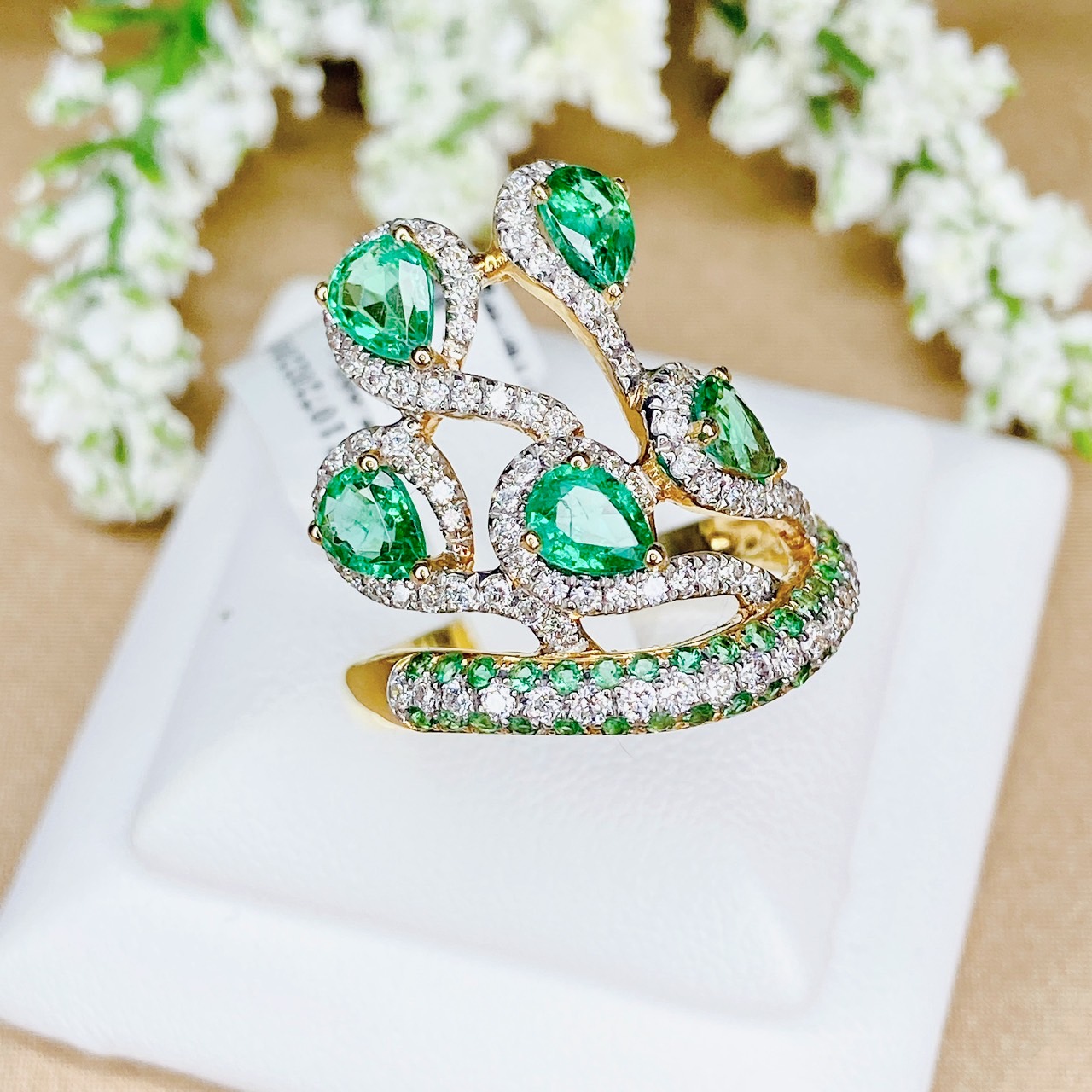 แหวนเพชรไขว้ล้อมมรกต The ring rotates upward. โดยฝังเพชรแถวสลับมรกตที่ตัวเรือนด้านล่าง แล้วค่อยหมุนไต่ระดับขึ้นด้านบนเป็นเหมือนสวนดอกไม้ Floral motif
