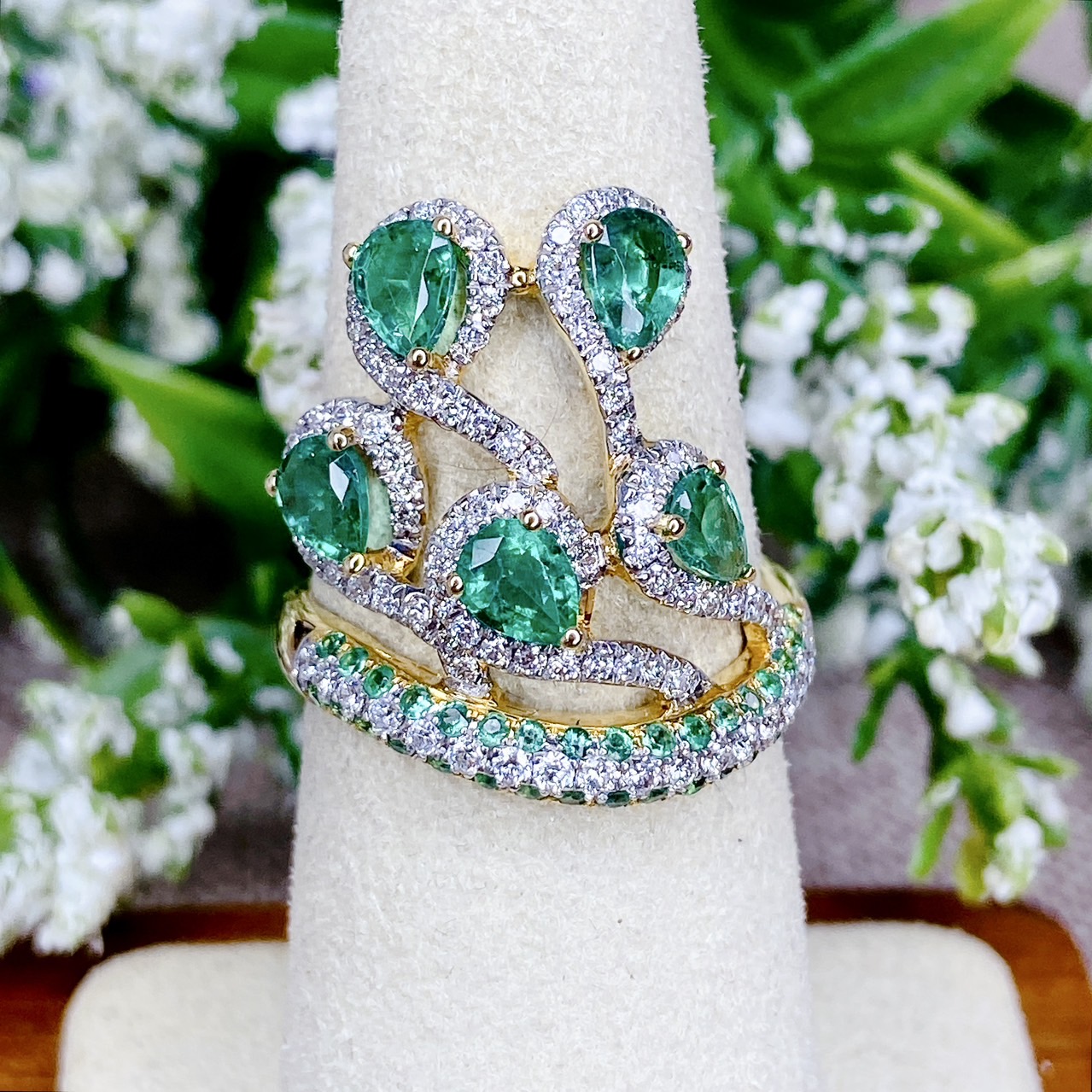 แหวนเพชรไขว้ล้อมมรกต The ring rotates upward. โดยฝังเพชรแถวสลับมรกตที่ตัวเรือนด้านล่าง แล้วค่อยหมุนไต่ระดับขึ้นด้านบนเป็นเหมือนสวนดอกไม้ Floral motif